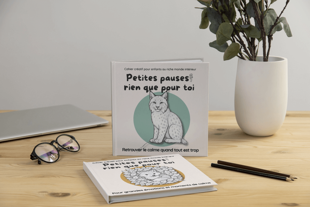 kleine-mutpausen (19) Aufgestelltes Exemplar des Kinderbuchs „Kleine Mutpausen – Für Tage, an denen alles zu viel ist“ mit Luchs-Cover, dahinter ein weiteres Buch mit Fuchs-Cover, auf Tisch mit Brille und Pflanze.